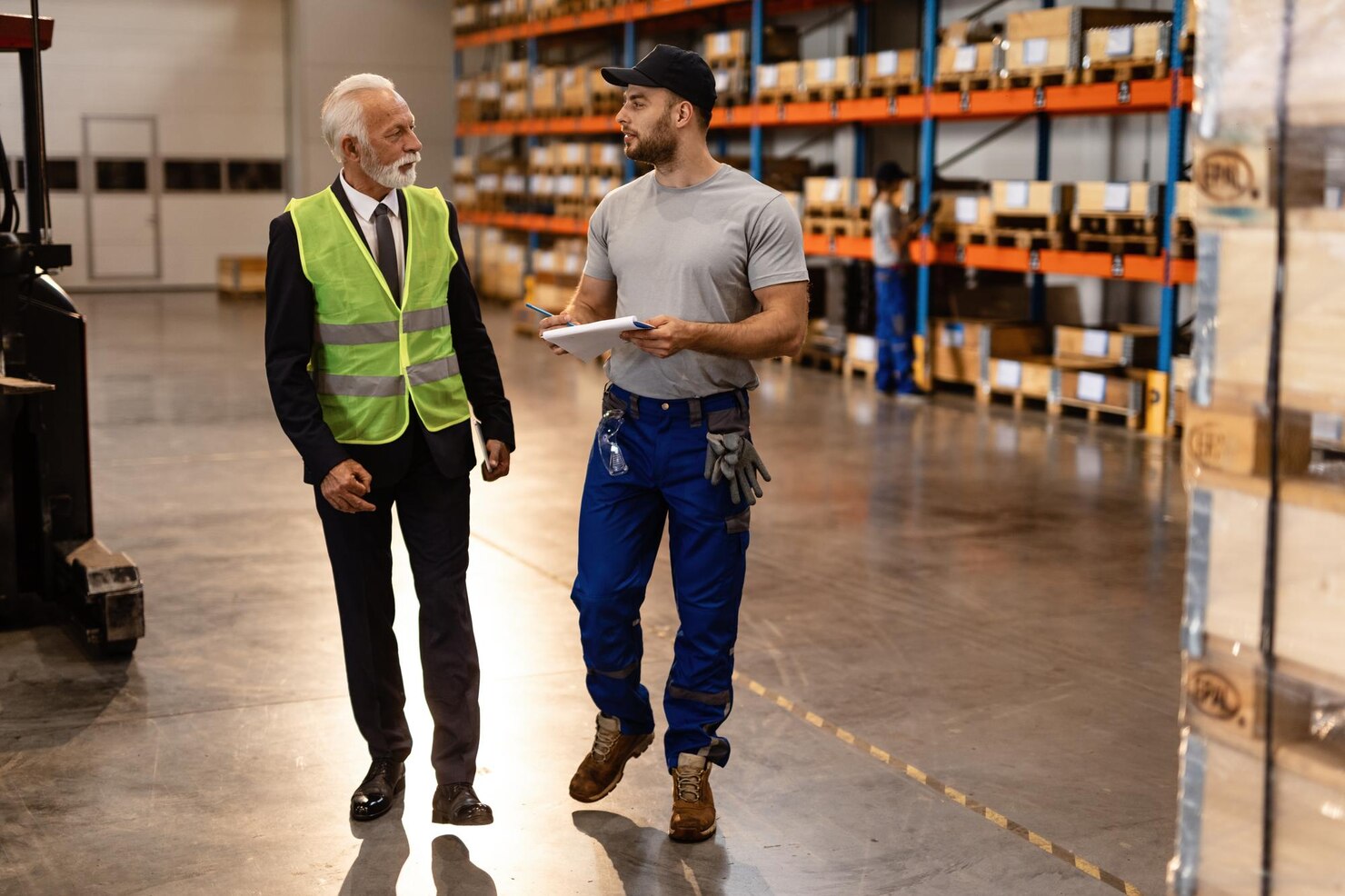 warehouse-worker-mature-businessman-talking-while-going-through-paperwork-industrial-building_637285-4194